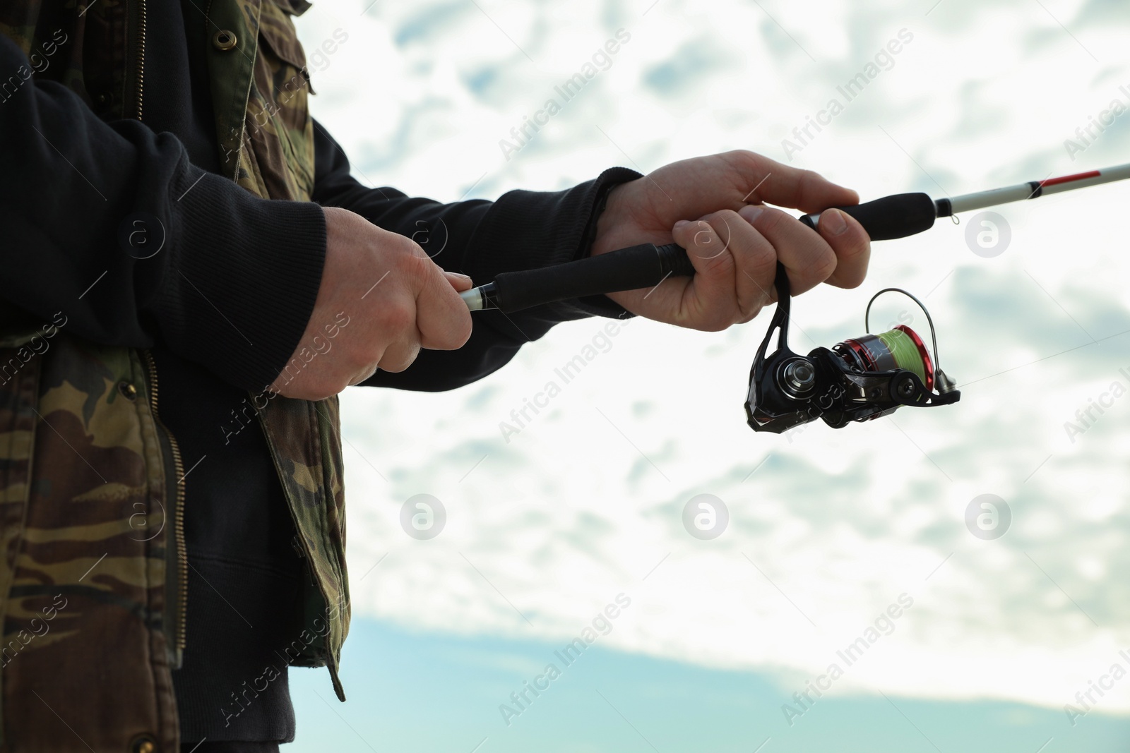 Photo of Fisherman with rod fishing under cloudy sky, closeup