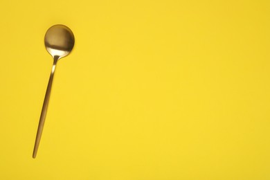 Photo of One shiny golden spoon on yellow background, top view. Space for text