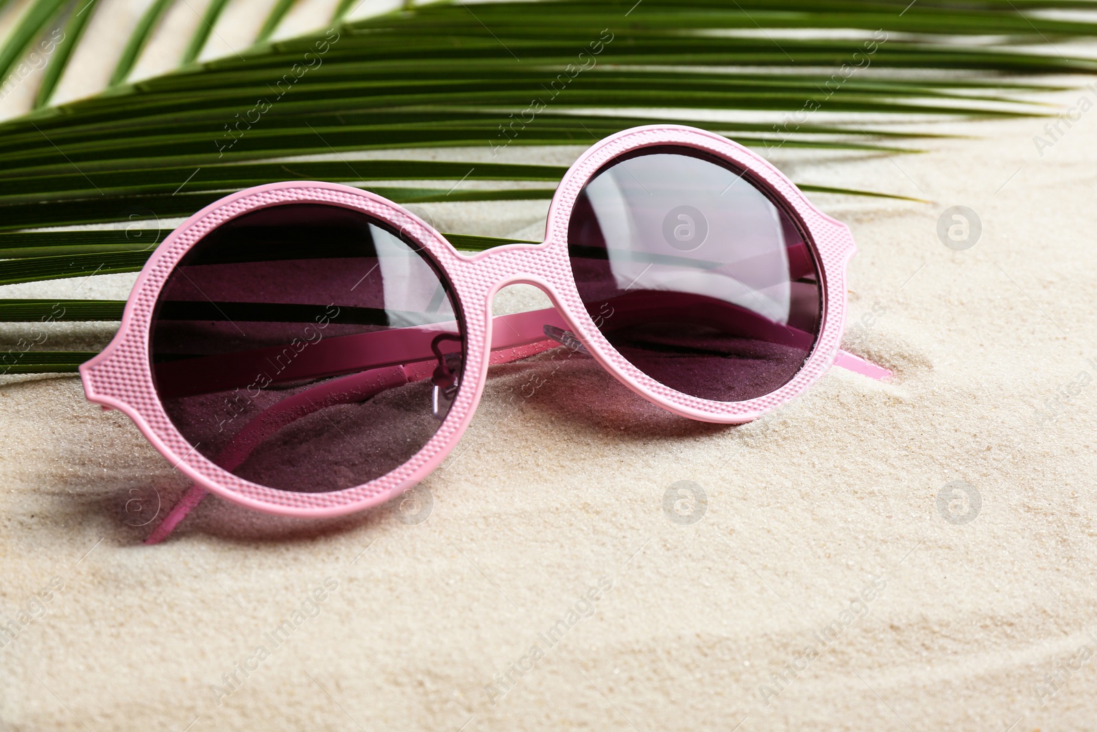 Photo of Stylish sunglasses and tropical leaf on white sand. Vacation time