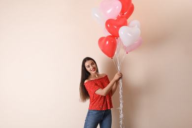 Beautiful young woman with heart shaped balloons on beige background. Valentine's day celebration
