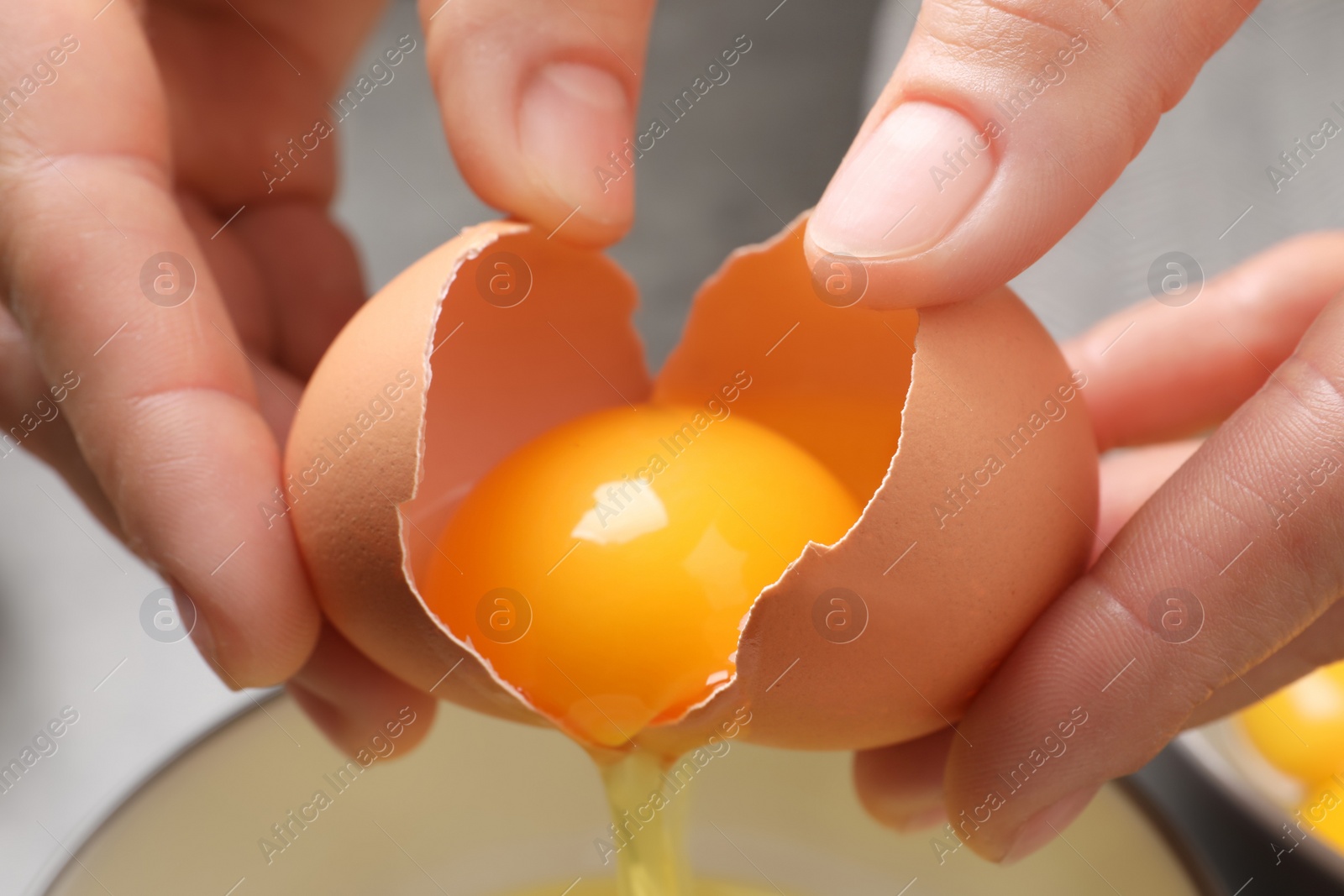 Photo of Woman separating egg yolk from white over bowl, closeup