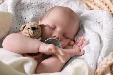 Photo of Cute newborn baby sleeping on white blanket in wicker crib, closeup