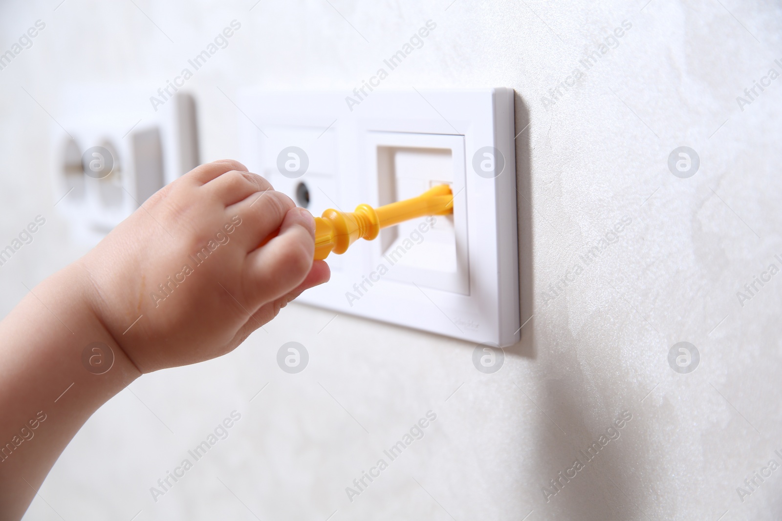 Photo of Little child playing with toy screwdriver and electrical socket indoors, closeup. Dangerous situation