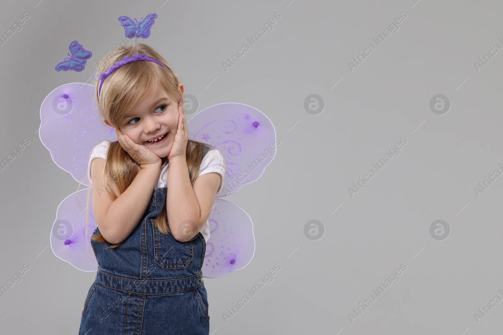 Photo of Cute little girl in fairy costume with violet wings on light grey background, space for text