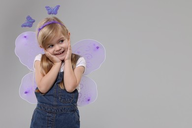Photo of Cute little girl in fairy costume with violet wings on light grey background, space for text