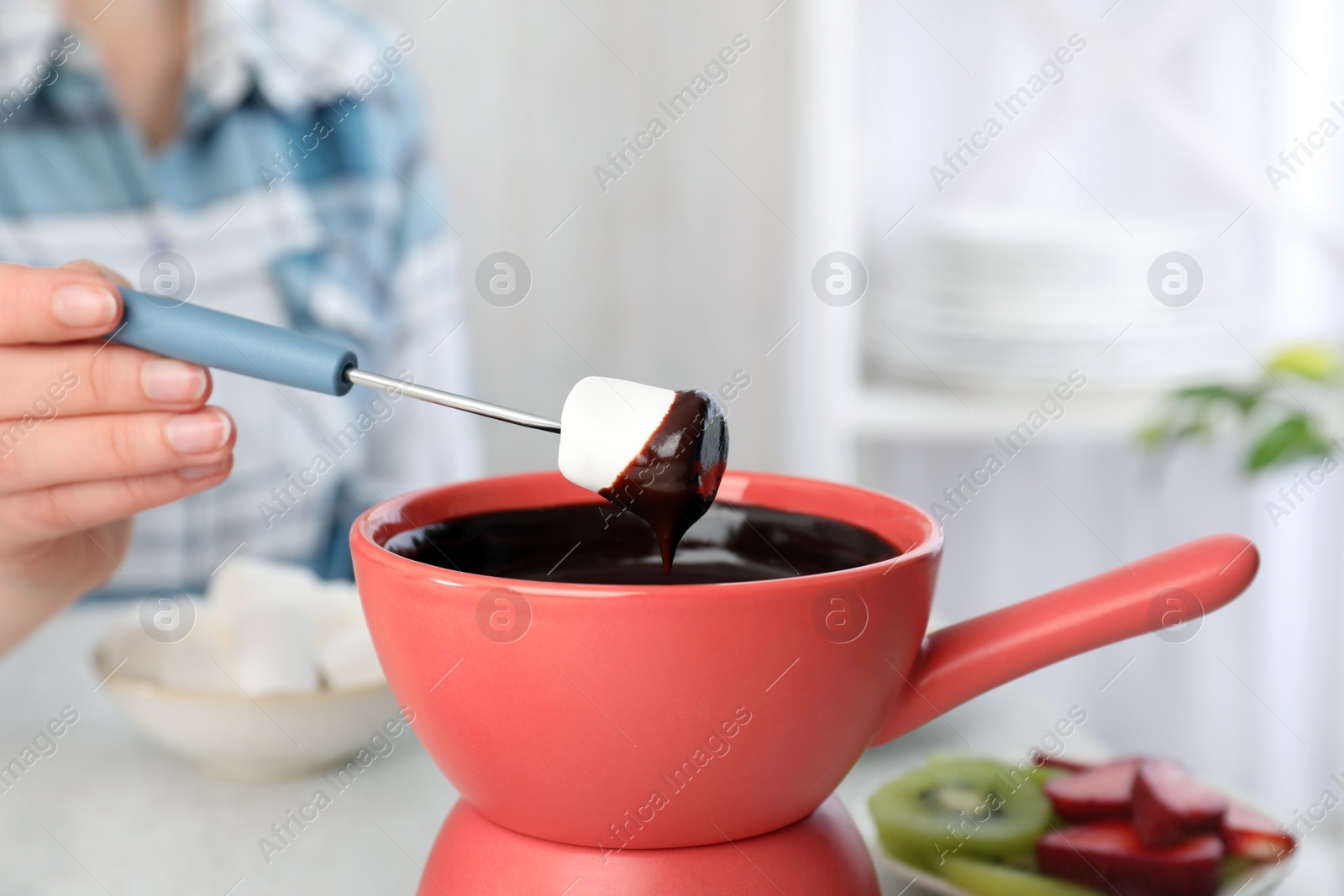 Photo of Woman dipping marshmallow into pot with chocolate fondue at table, closeup