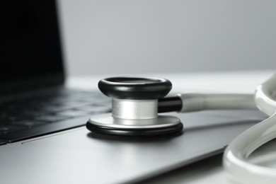 Modern laptop and stethoscope on white table, closeup