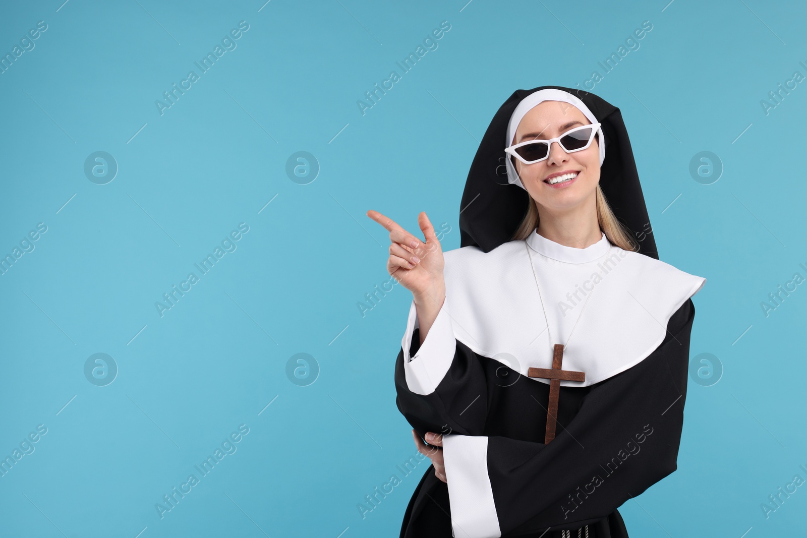 Photo of Happy woman in nun habit pointing at something against light blue background. Space for text