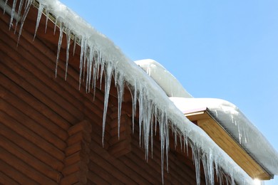 House with icicles on roof, low angle view. Winter season