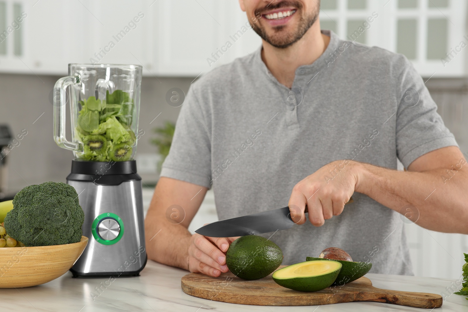 Photo of Man cutting avocado for delicious smoothie at white marble table in kitchen, closeup