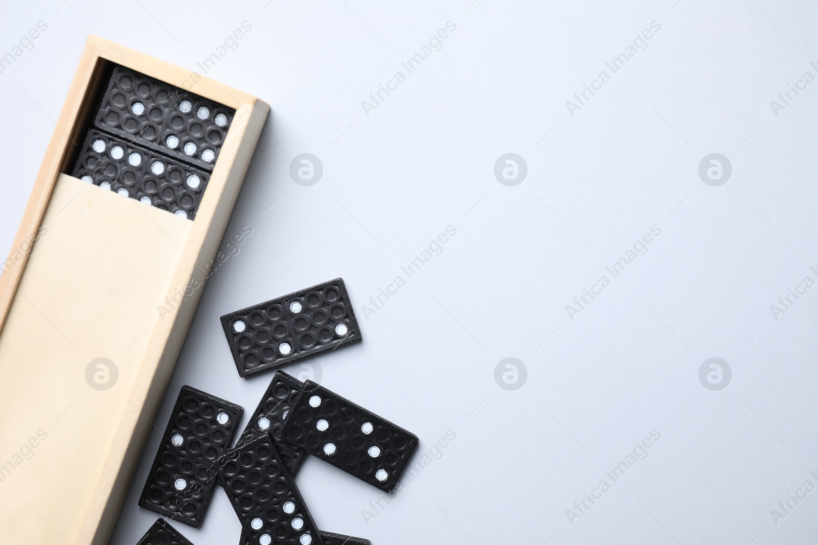 Photo of Wooden box with black domino tiles on white background, top view