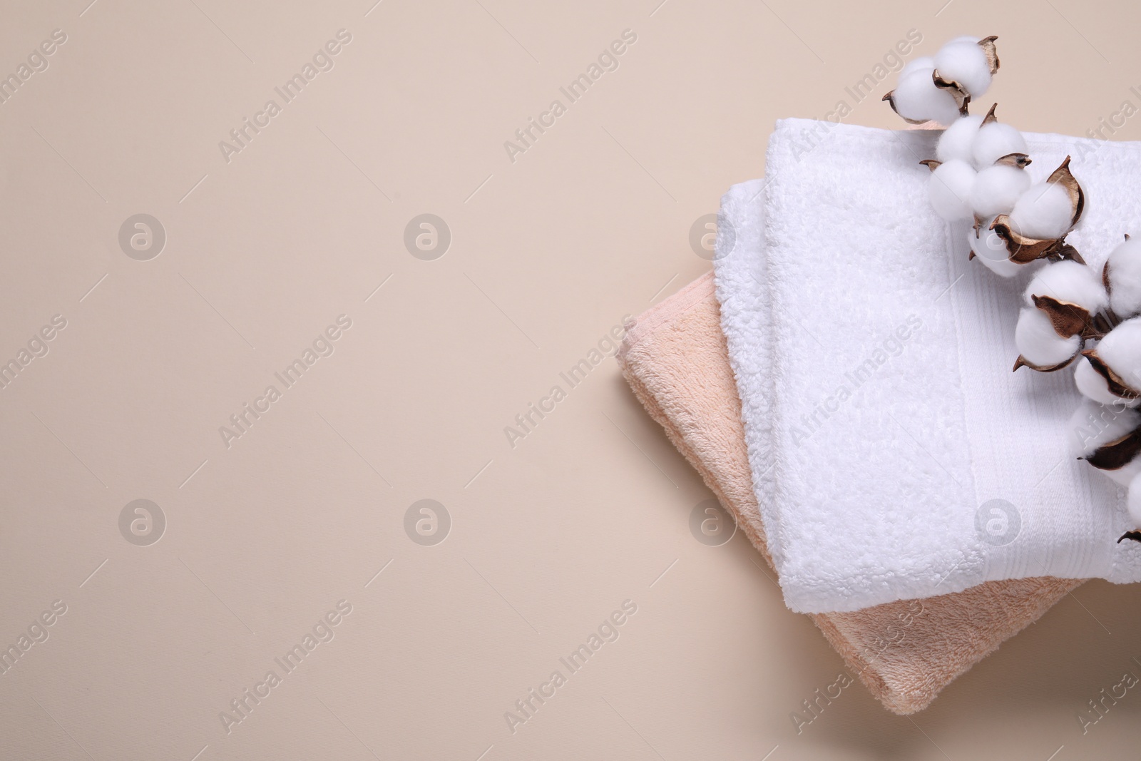 Photo of Cotton branch with fluffy flowers and terry towels on beige background, top view. Space for text