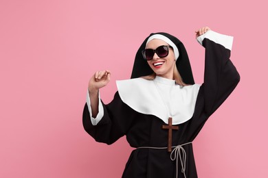 Photo of Happy woman in nun habit and sunglasses against pink background. Space for text