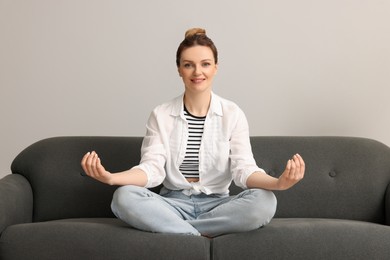 Woman meditating on sofa near light grey wall. Harmony and zen