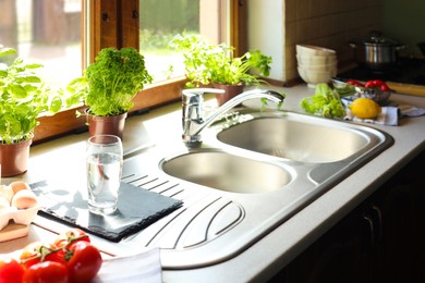 Photo of Kitchen counter with sink, potted herbs and fresh products near window on sunny morning