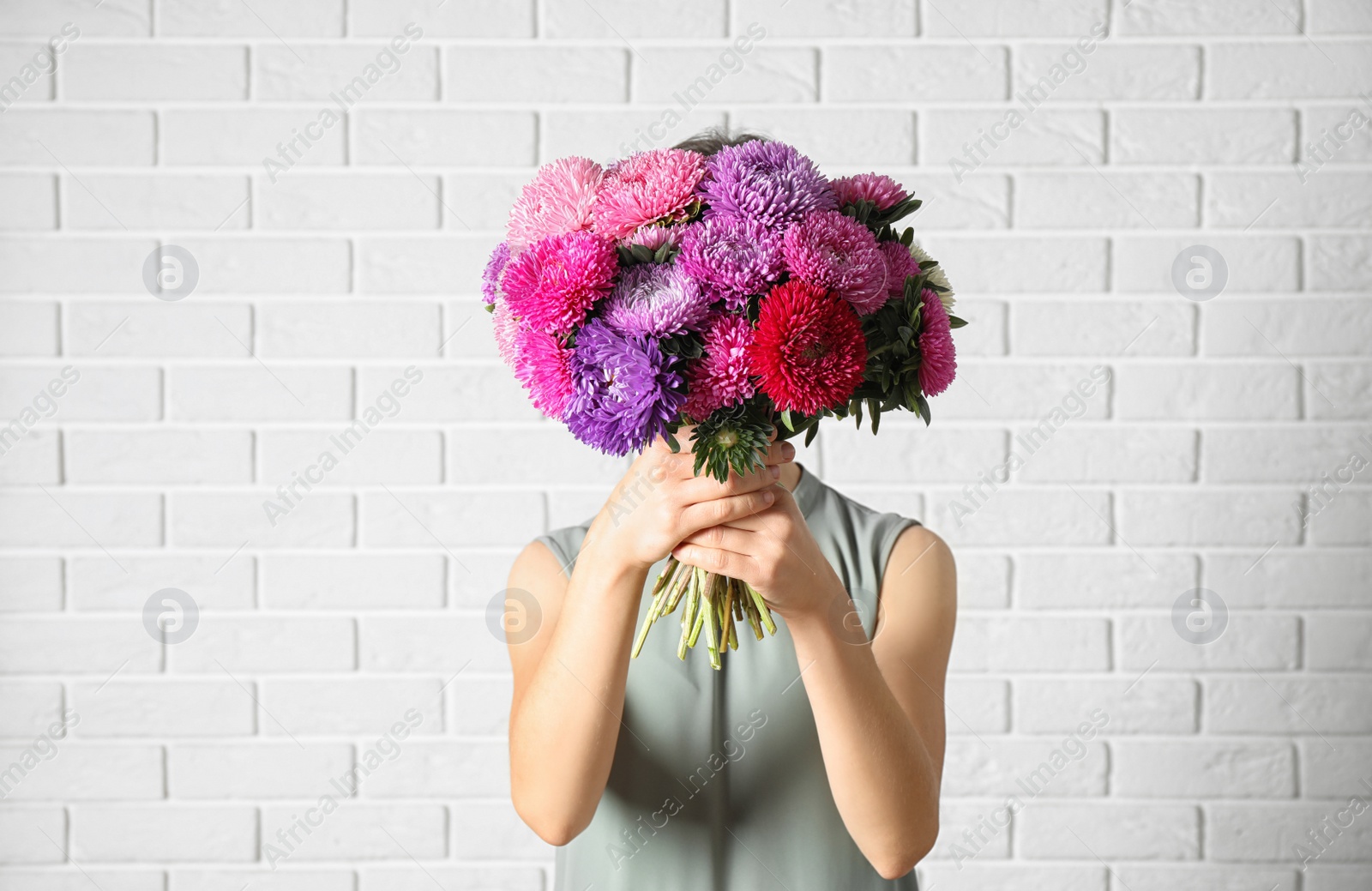 Photo of Woman holding bouquet of beautiful aster flowers against white brick wall