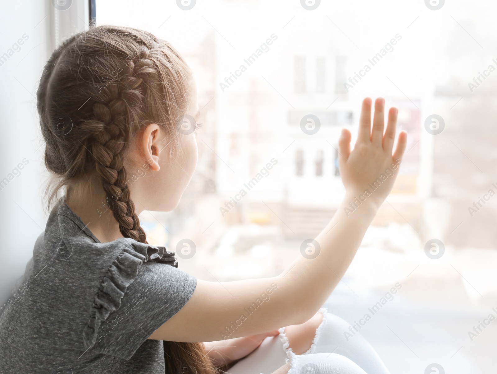 Photo of Lonely little girl near window indoors. Child autism