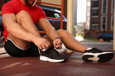 Photo of Man tying shoelaces before training at outdoor gym on sunny day, closeup