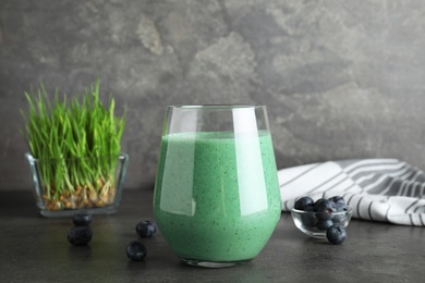 Glass of spirulina smoothie and fresh blueberries on table against grey background