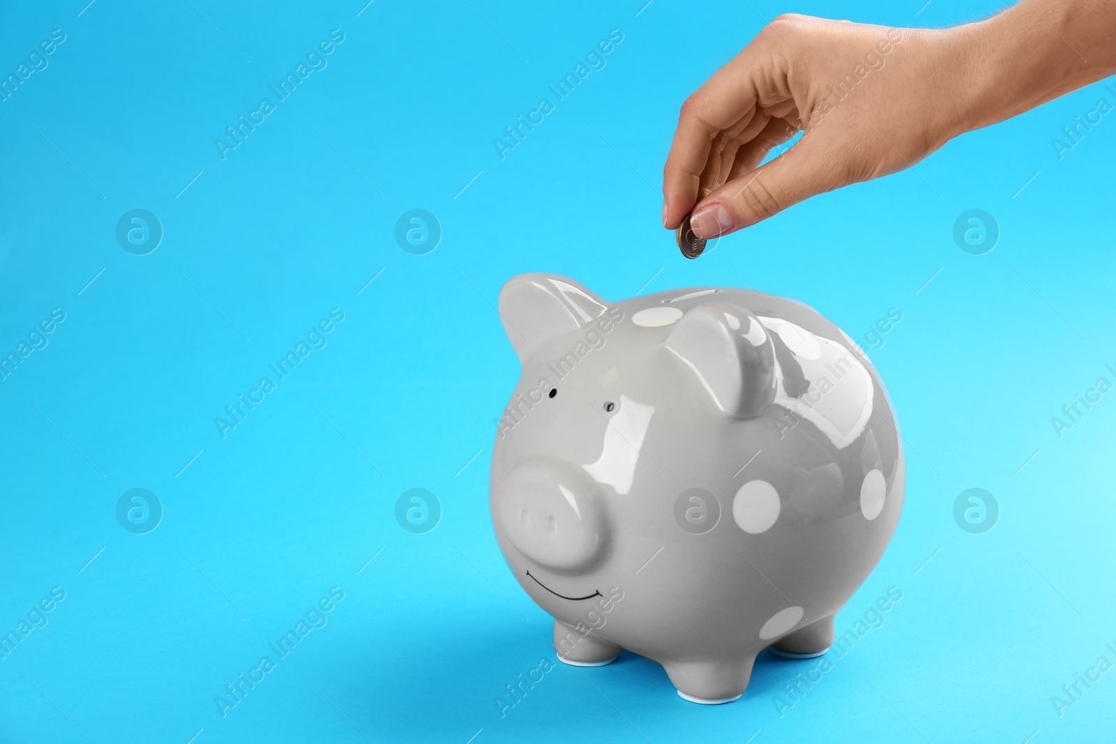 Photo of Woman putting coin into piggy bank on blue background, closeup