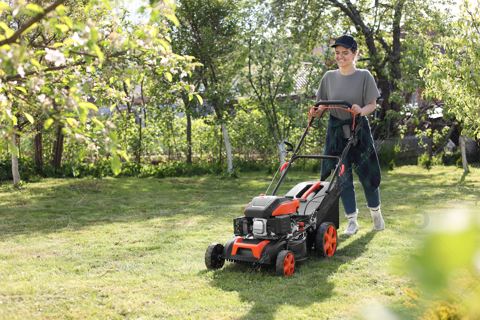 Photo of Smiling woman cutting green grass with lawn mower in garden