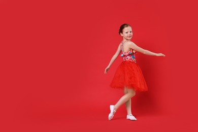 Photo of Cute little girl dancing on red background, space for text