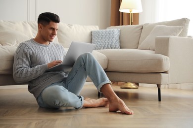 Photo of Man with laptop sitting on warm floor in living room. Heating system