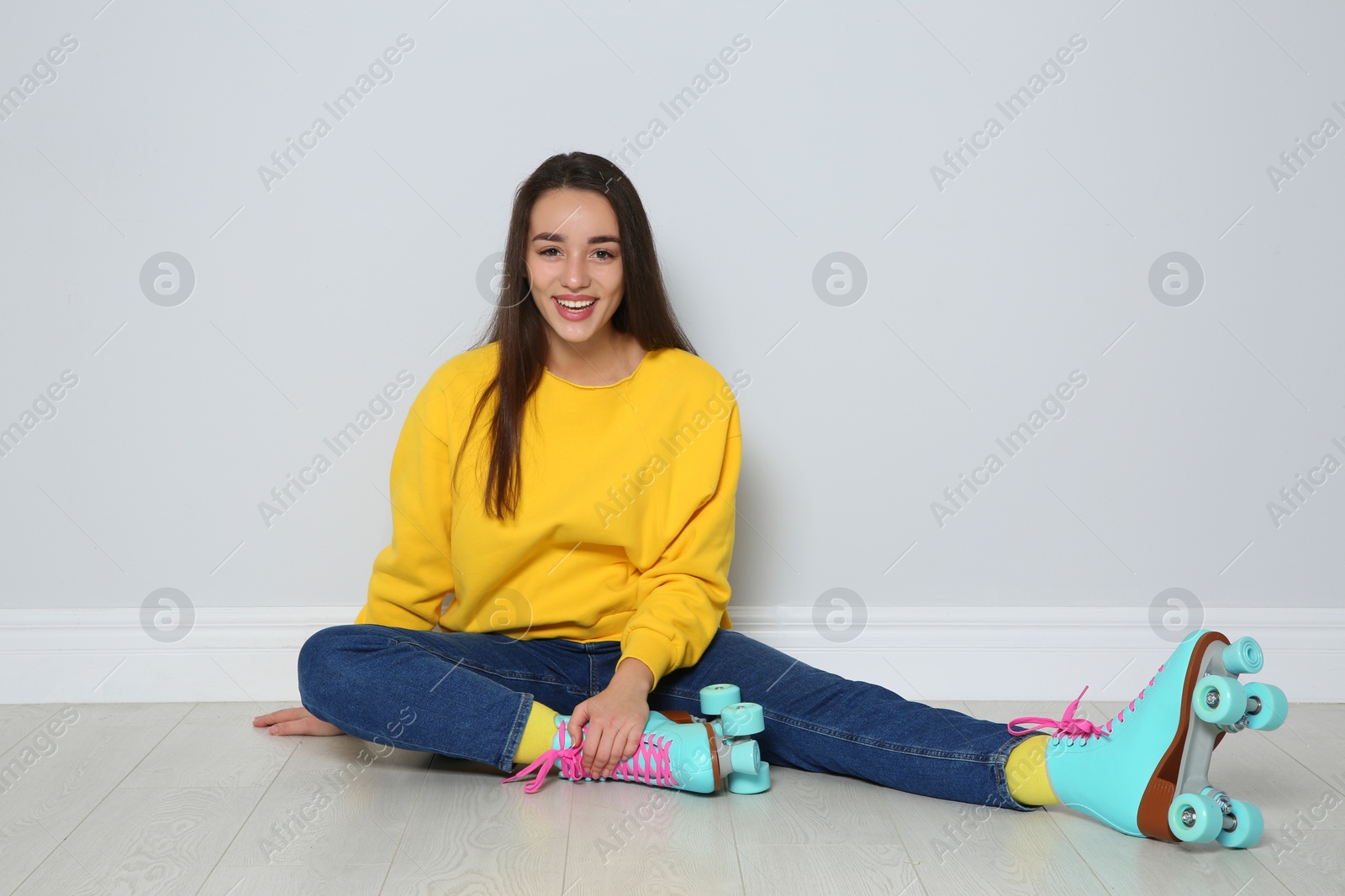 Photo of Young woman with roller skates sitting on floor near color wall