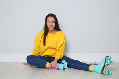 Young woman with roller skates sitting on floor near color wall