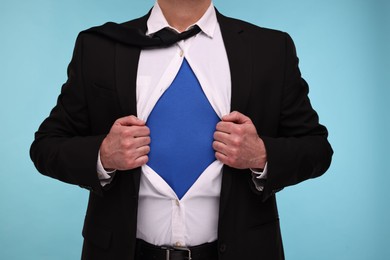 Businessman wearing superhero costume under suit on light blue background, closeup