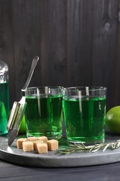 Photo of Absinthe in glasses, rosemary, brown sugar and spoon on table. Alcoholic drink