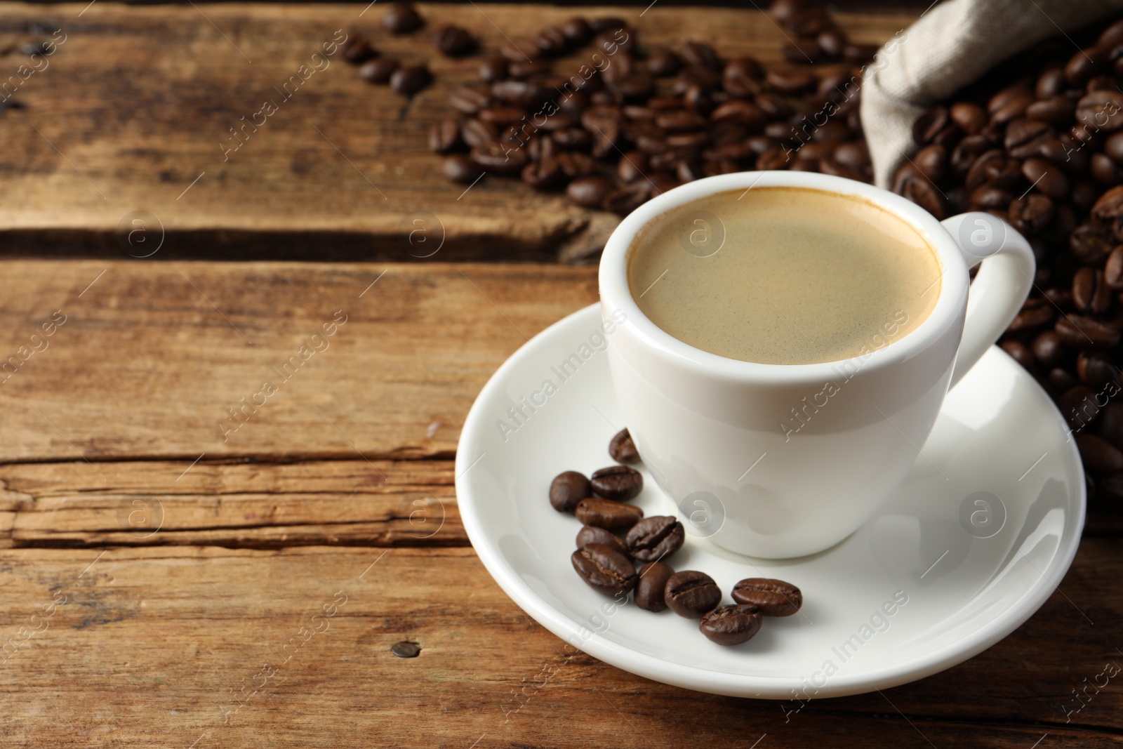 Photo of Cup of hot aromatic coffee and roasted beans on wooden table, space for text