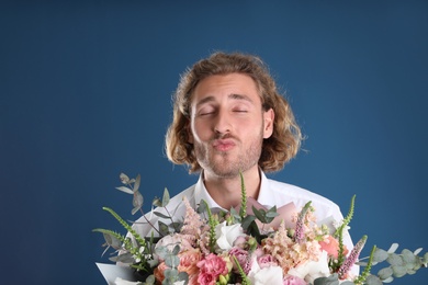 Photo of Young handsome man with beautiful flower bouquet on blue background