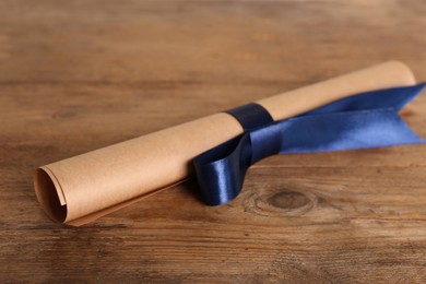 Photo of Rolled student's diploma with blue ribbon on wooden table