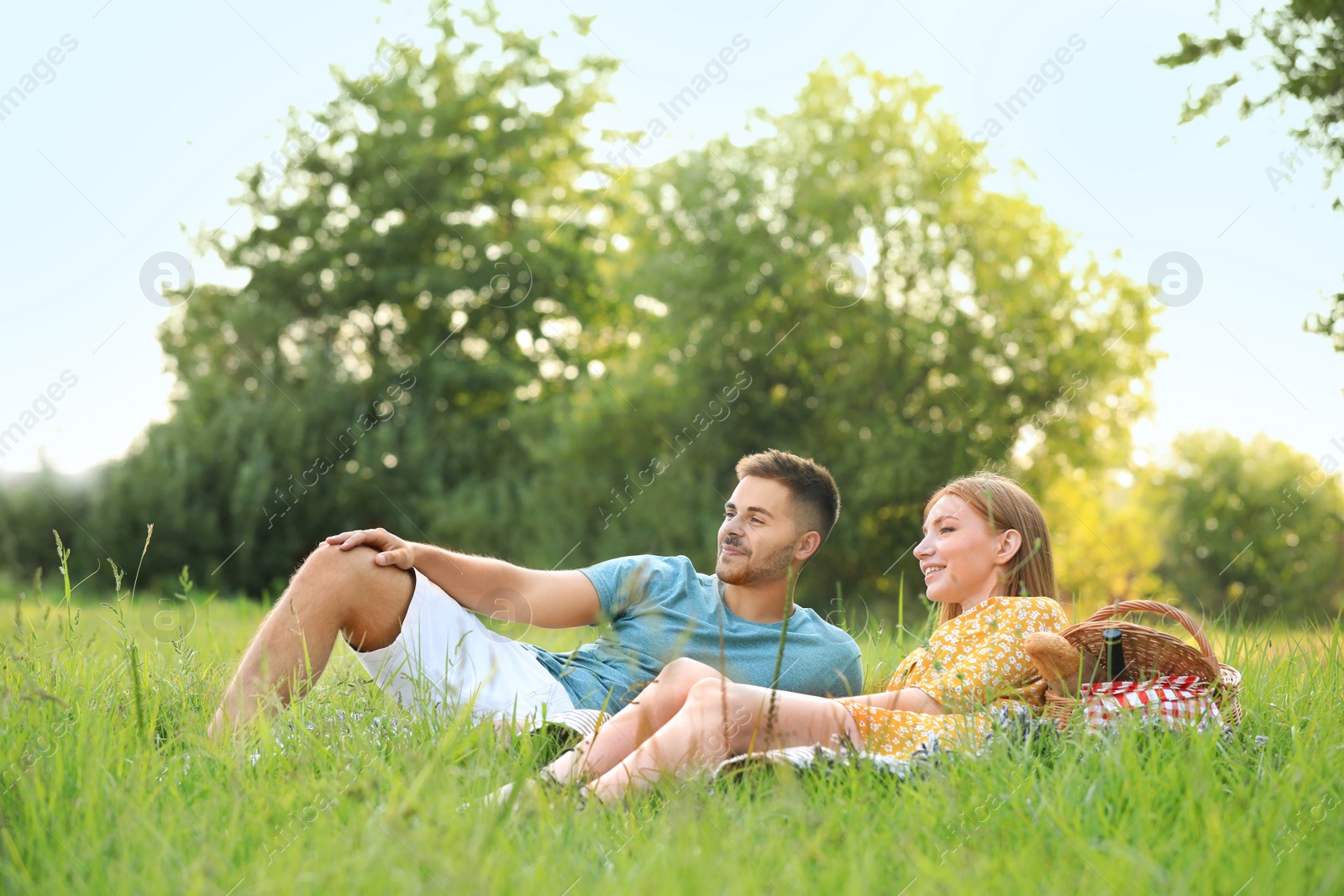 Photo of Happy young couple having picnic on green grass in park