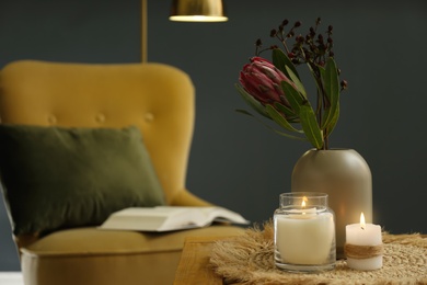 Vase with beautiful protea flowers and burning candles on wooden table indoors, space for text. Interior elements