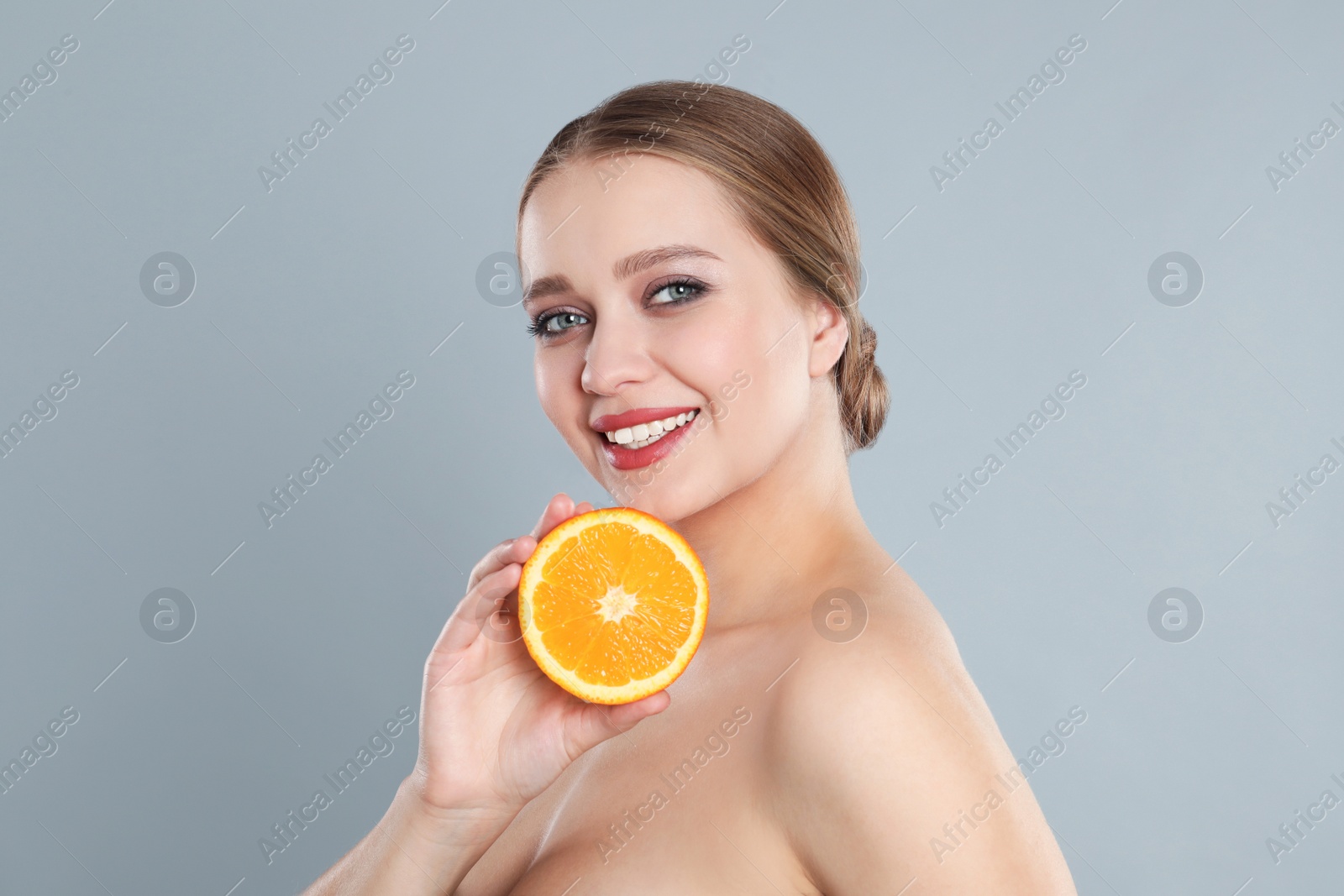 Photo of Young woman with cut orange on grey background. Vitamin rich food