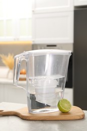 Photo of Water filter jug and lime on light table in kitchen, closeup