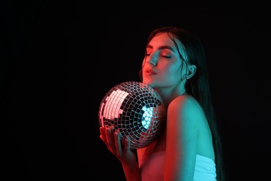 Photo of Beautiful woman with disco ball posing in neon lights against black background. Space for text