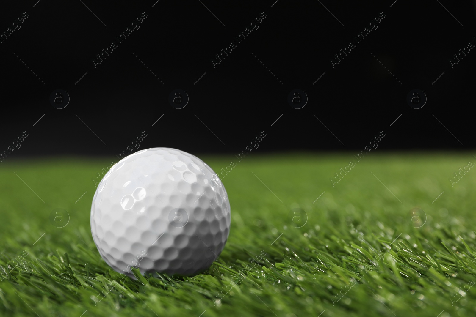 Photo of Golf ball on green grass against black background, space for text