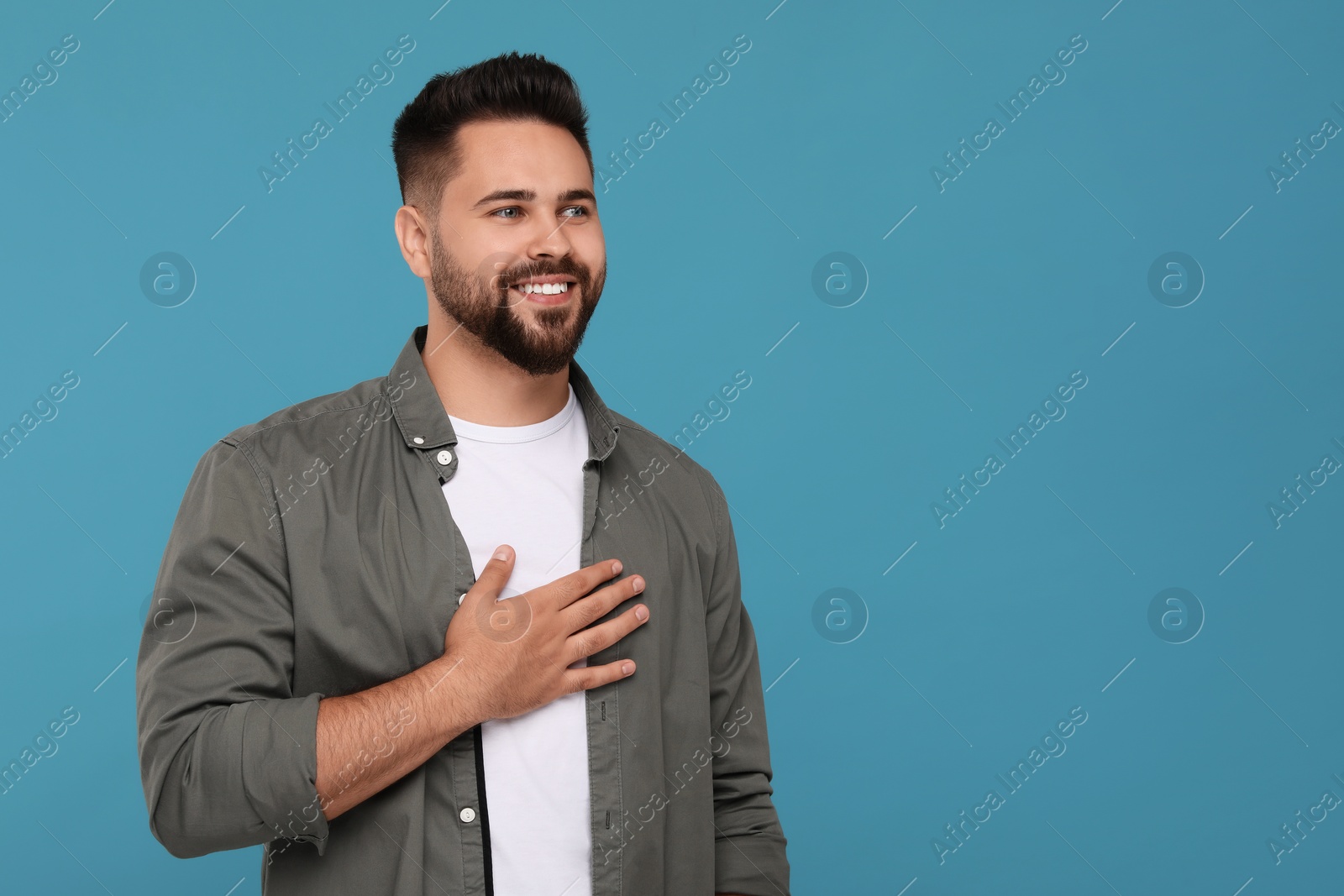 Photo of Thank you gesture. Happy grateful man with hand on chest against light blue background, space for text