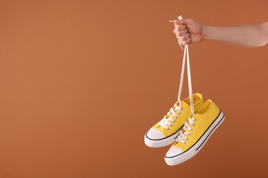 Photo of Woman holding pair of yellow classic old school sneakers on brown background, closeup. Space for text