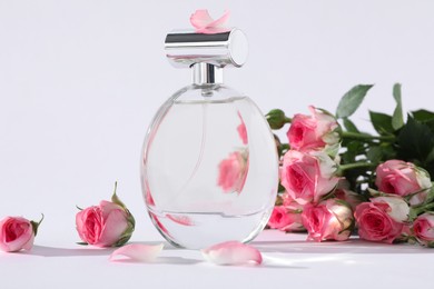 Photo of Bottle of luxury perfume and beautiful roses on white background. Floral fragrance