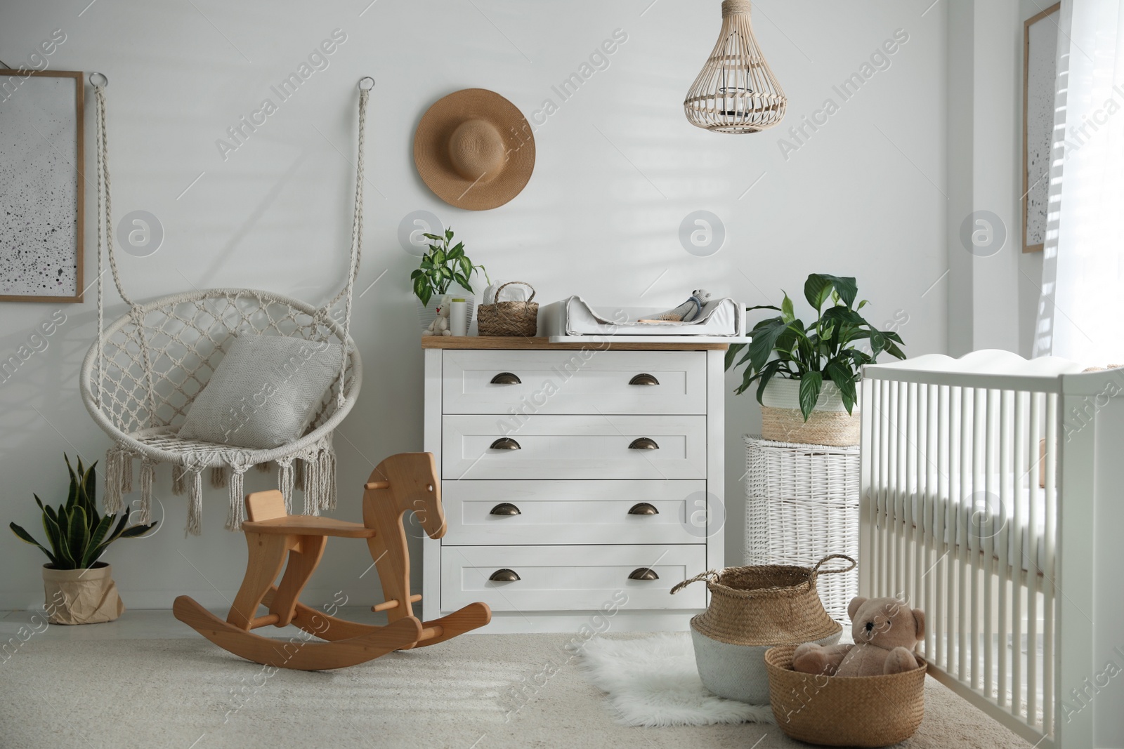 Photo of Chest of drawers with changing tray and pad near comfortable cradle in baby room. Interior design