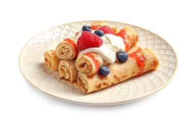 Thin pancakes with syrup, cream and berries on plate against white background