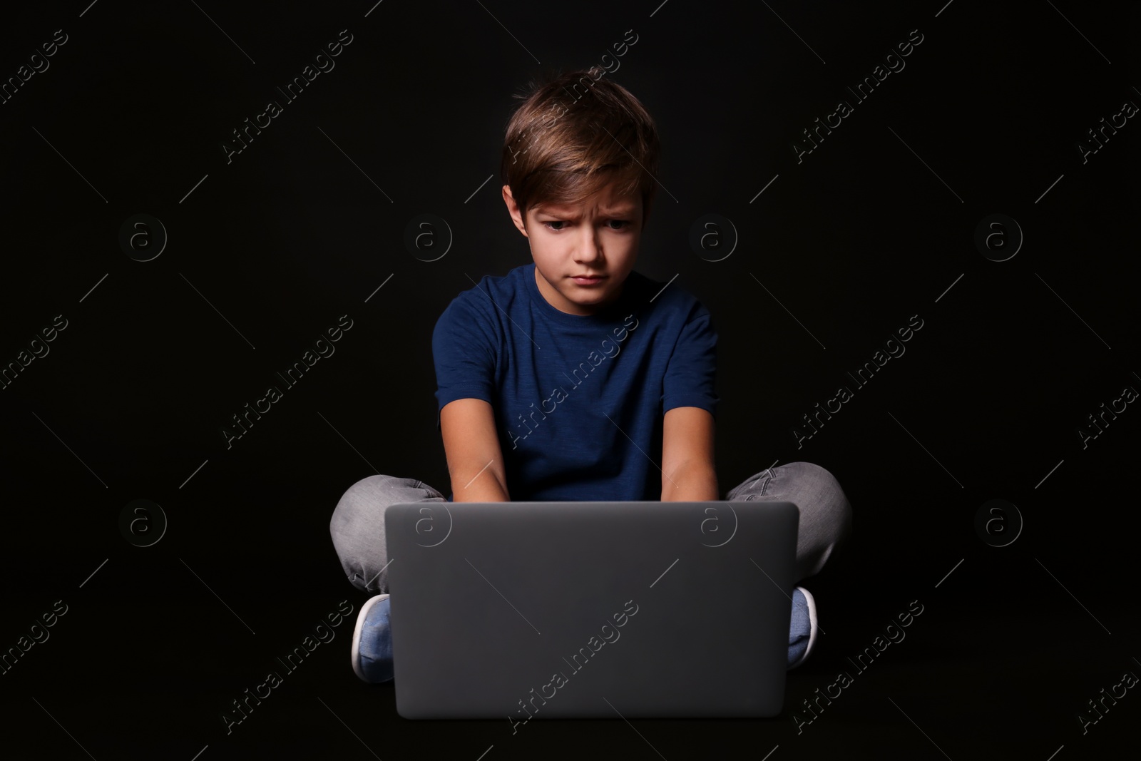 Photo of Shocked child with laptop on black background. Danger of internet