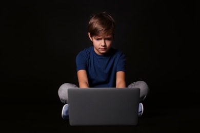 Shocked child with laptop on black background. Danger of internet