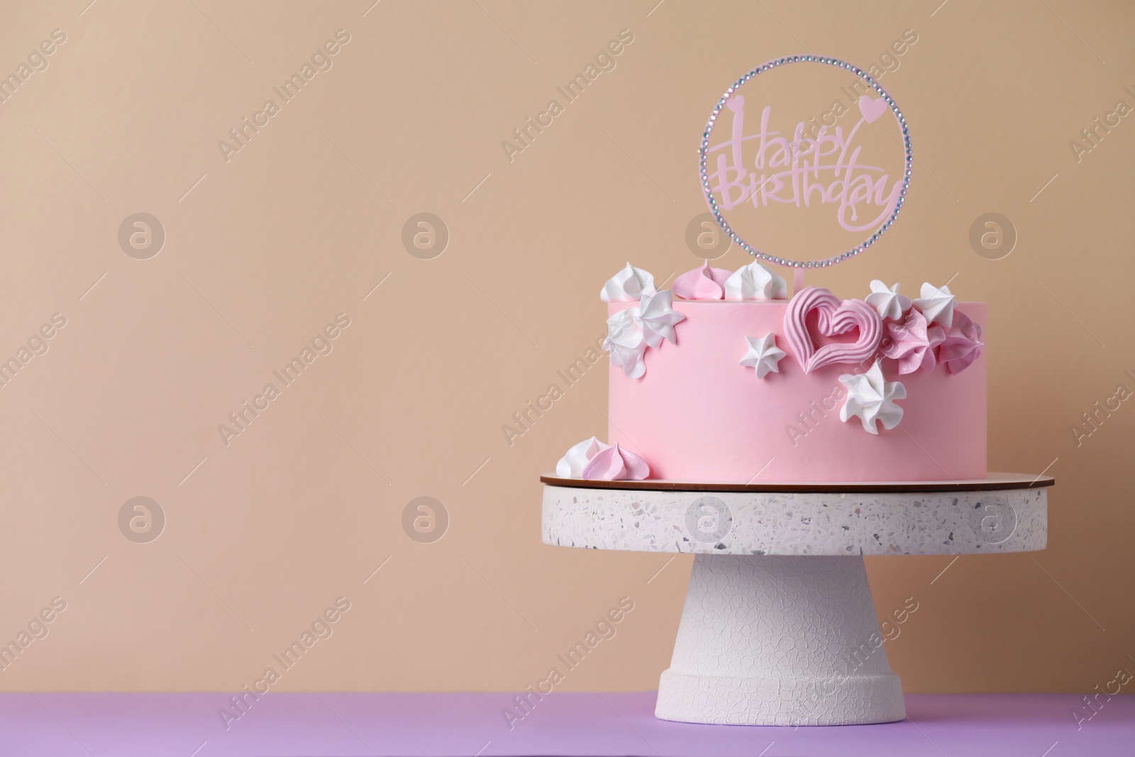 Photo of Beautifully decorated birthday cake on violet table near beige wall, space for text