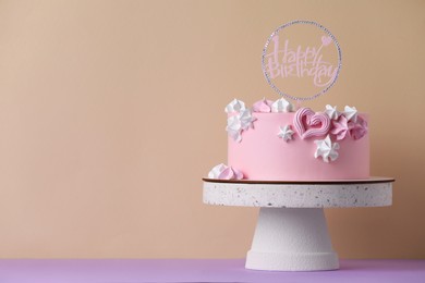 Photo of Beautifully decorated birthday cake on violet table near beige wall, space for text