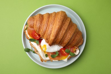 Photo of Tasty croissant with fried egg, tomato and microgreens on green background, top view
